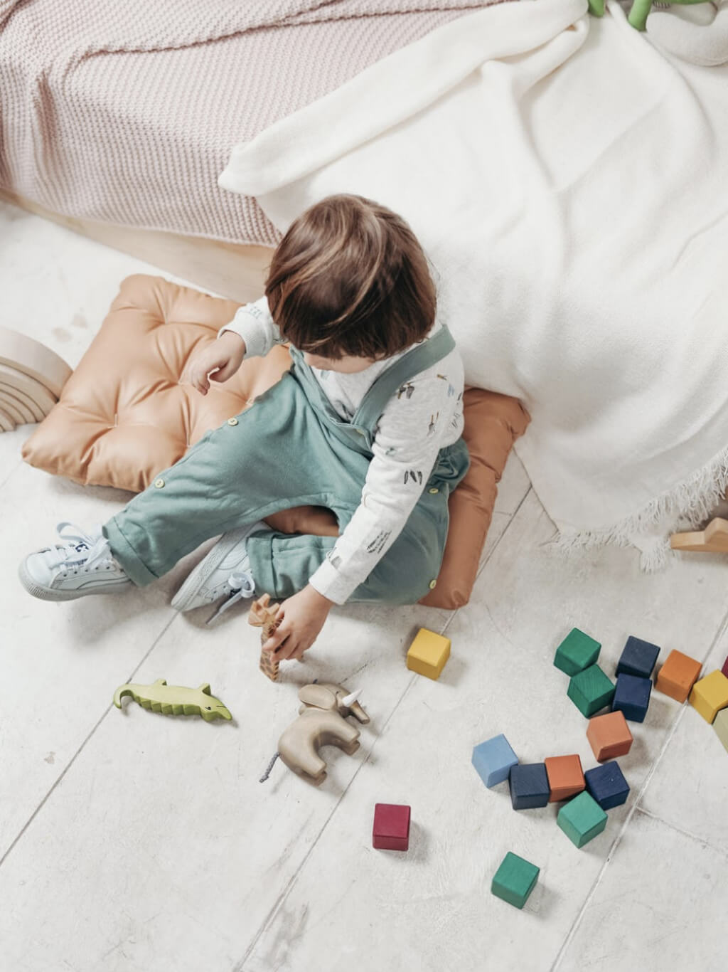 A child in overalls playing with colourful wooden blocks on the floor.